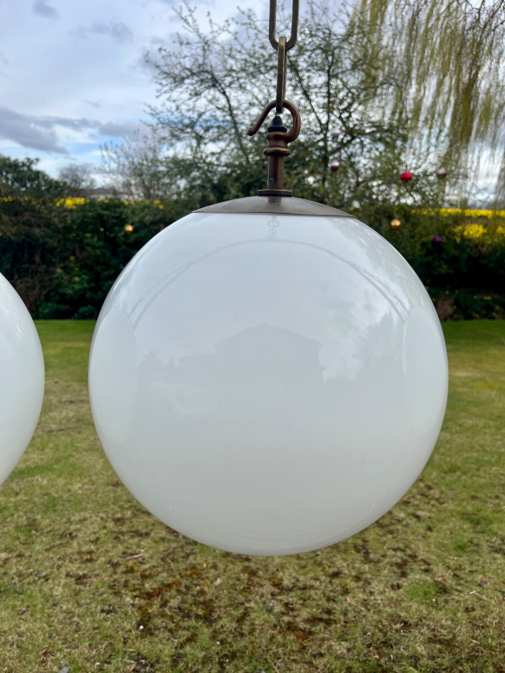 A set of three large white spherical opaline glass globe pendant lights suspended from dark metal chains. View X