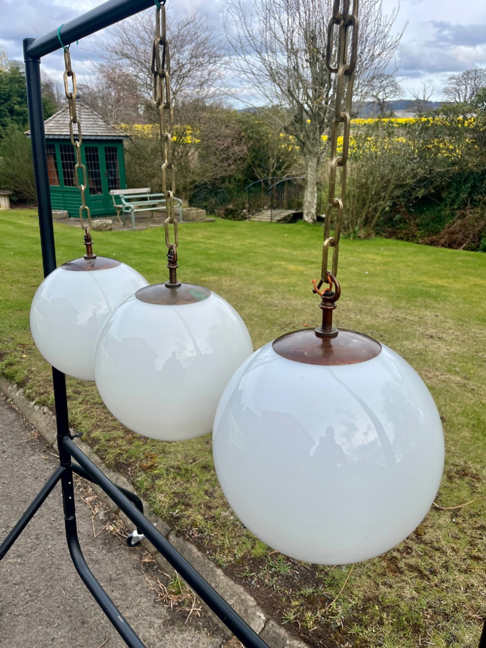 A set of three large white spherical opaline glass globe pendant lights suspended from dark metal chains. View XII