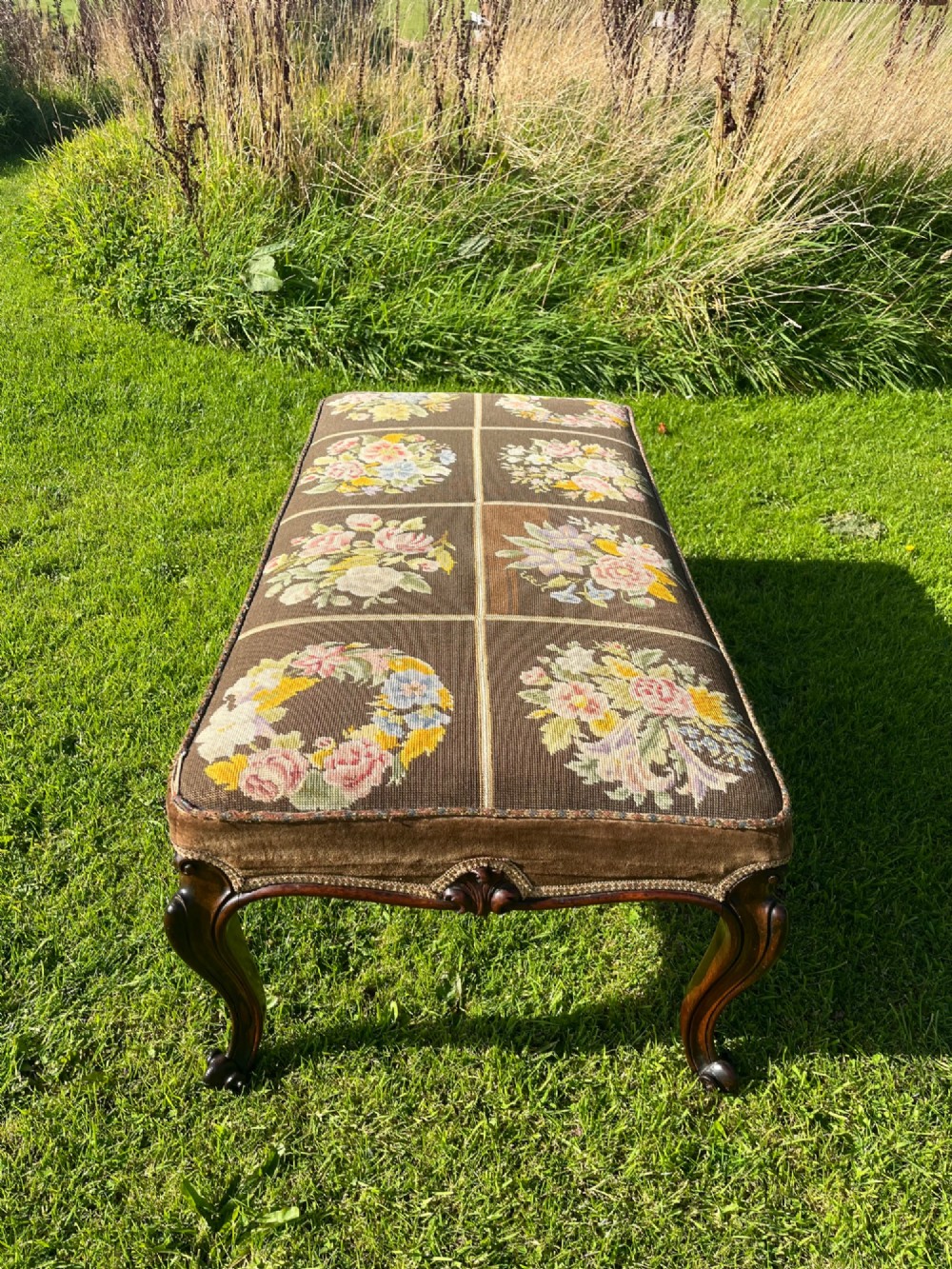 A long rectangular Victorian centre stool with dark rosewood cabriole legs and floral tapestry upholstery set in brown velvet. View V