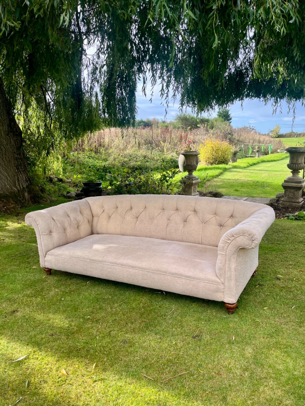 A Victorian style deep-seated sofa featuring button-tufted back upholstery in light beige fabric with turned wooden front legs.