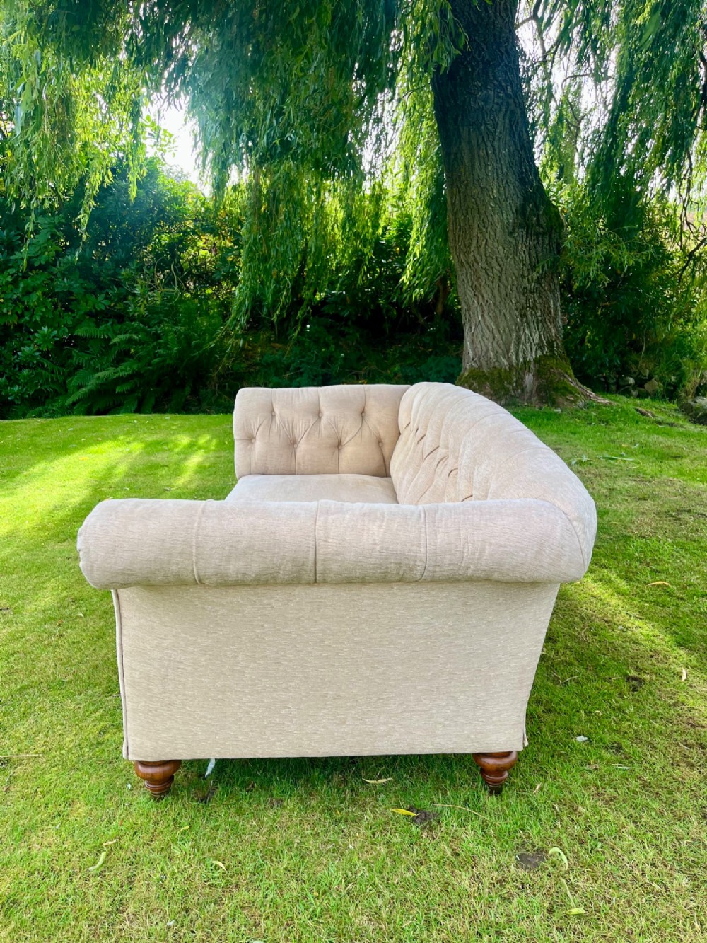 A Victorian style deep-seated sofa featuring button-tufted back upholstery in light beige fabric with turned wooden front legs. View II