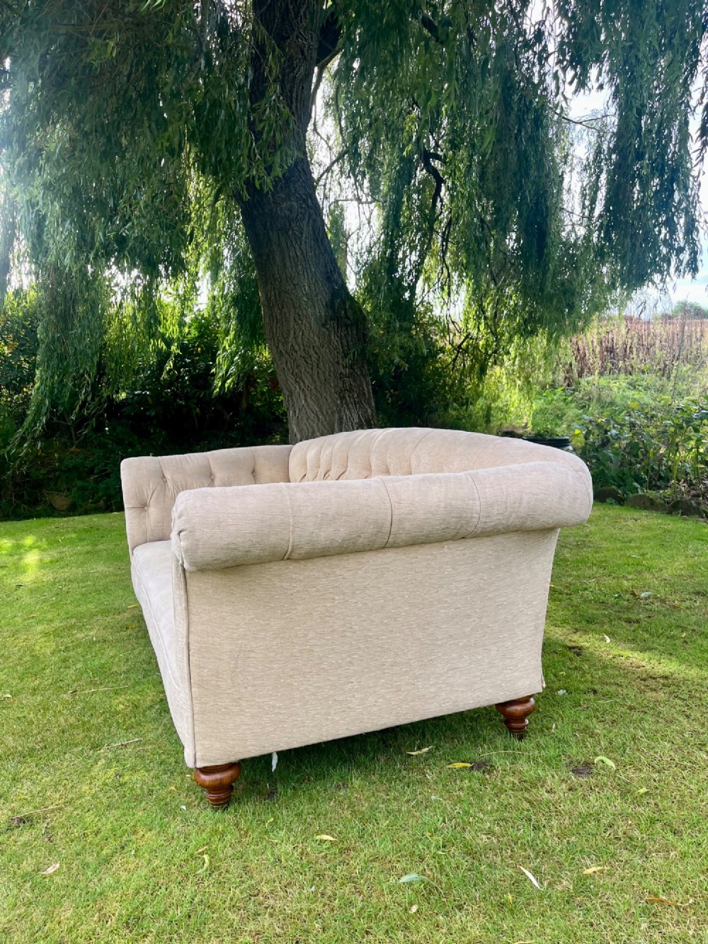 A Victorian style deep-seated sofa featuring button-tufted back upholstery in light beige fabric with turned wooden front legs. View III