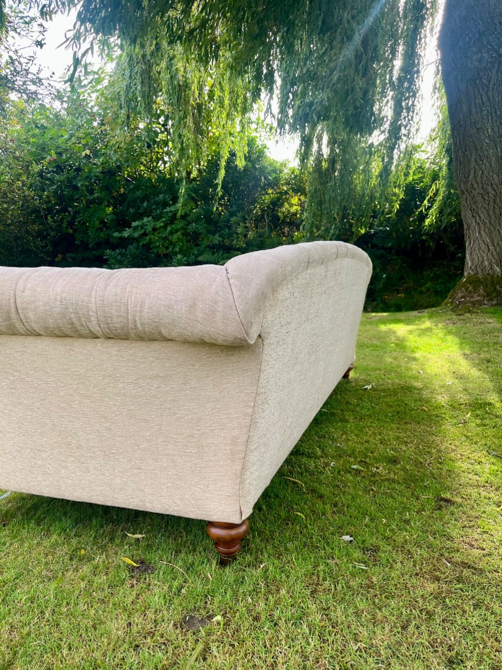 A Victorian style deep-seated sofa featuring button-tufted back upholstery in light beige fabric with turned wooden front legs. View IV