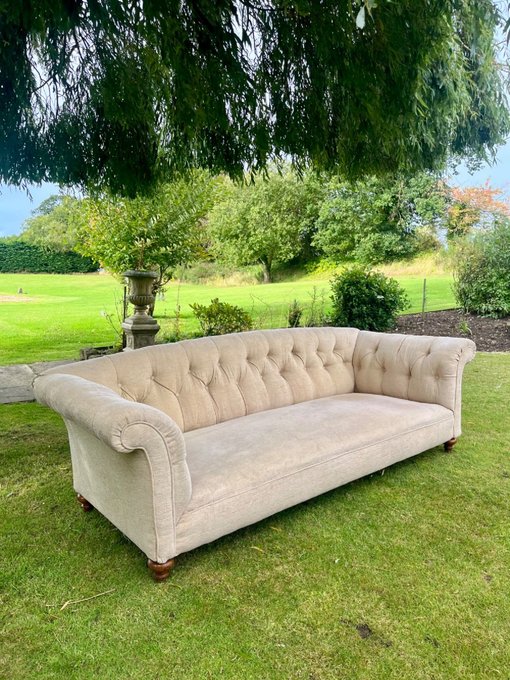 A Victorian style deep-seated sofa featuring button-tufted back upholstery in light beige fabric with turned wooden front legs. View V
