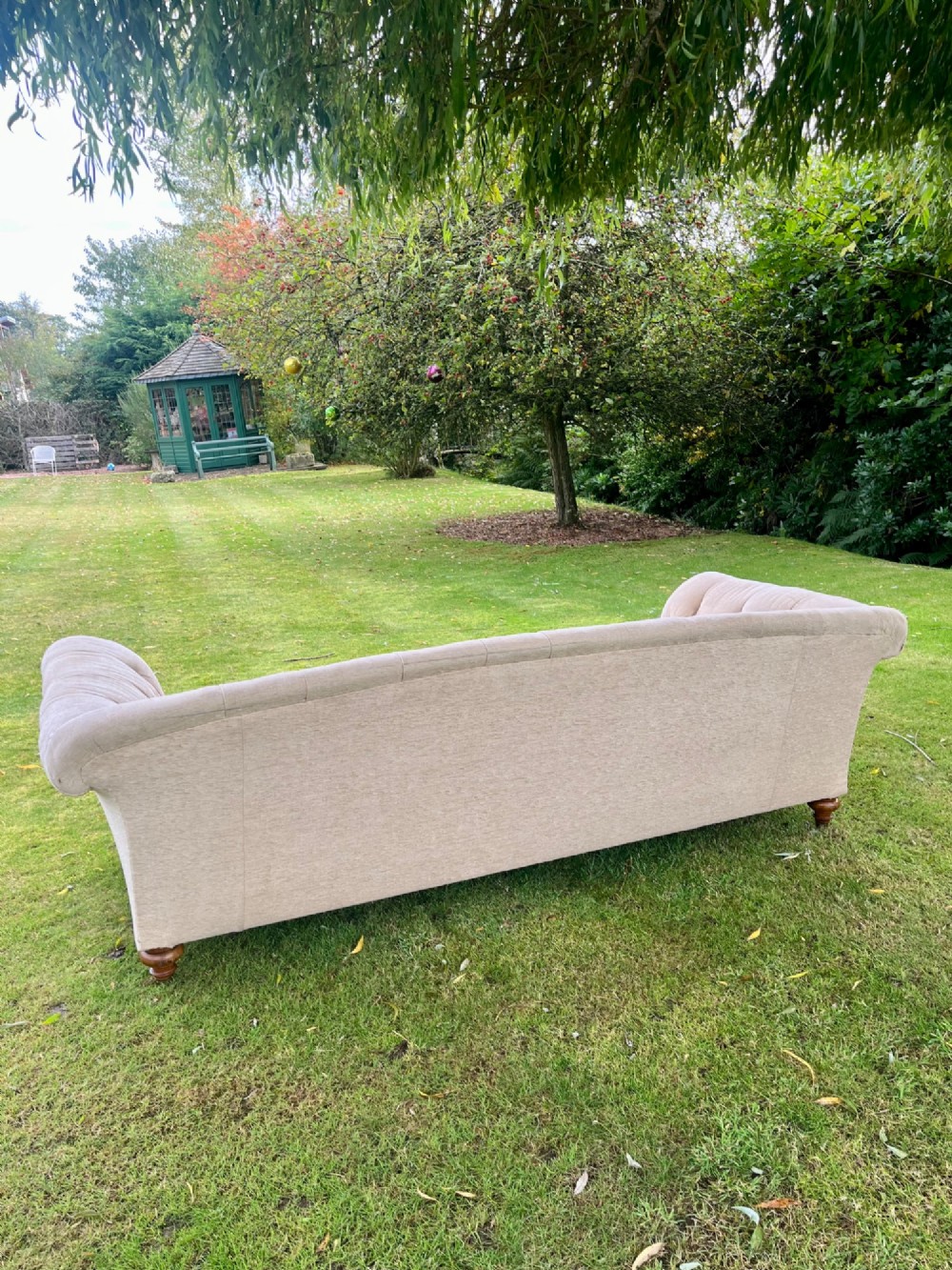 A Victorian style deep-seated sofa featuring button-tufted back upholstery in light beige fabric with turned wooden front legs. View VI