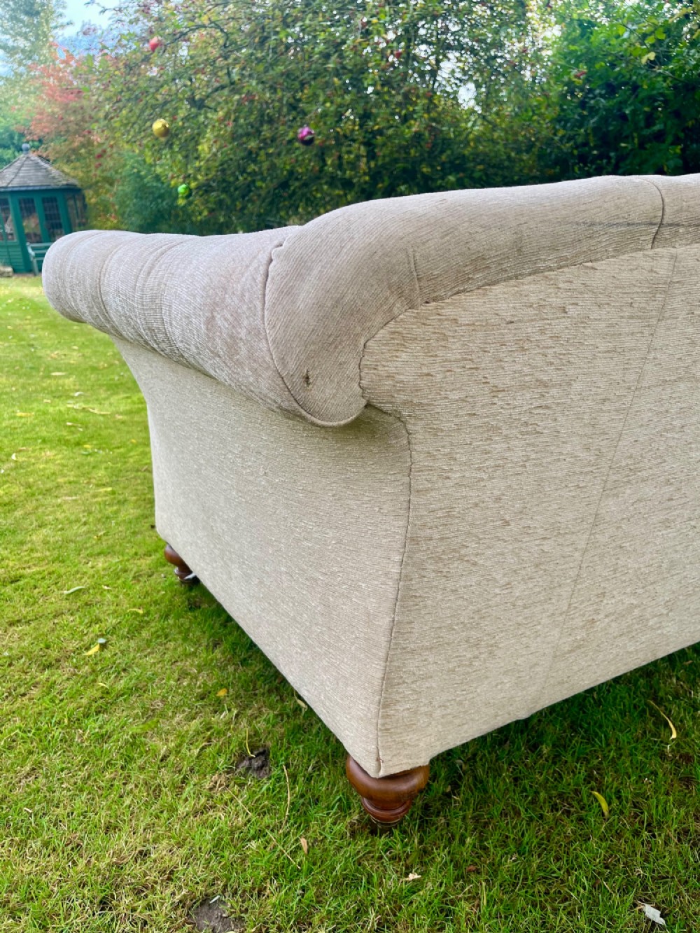 A Victorian style deep-seated sofa featuring button-tufted back upholstery in light beige fabric with turned wooden front legs. View VII