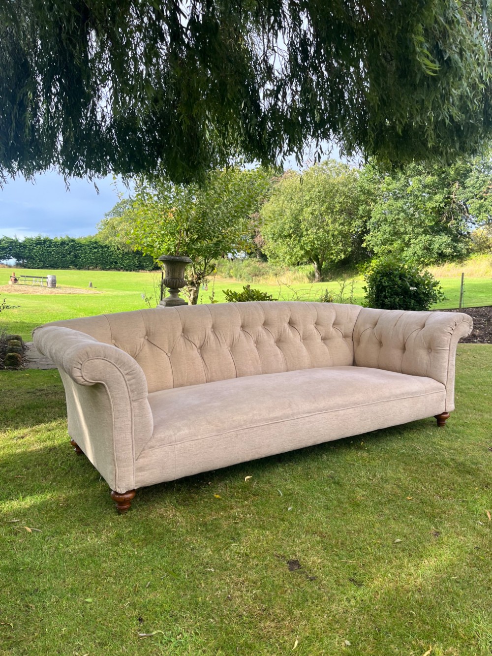 A Victorian style deep-seated sofa featuring button-tufted back upholstery in light beige fabric with turned wooden front legs. View XIV