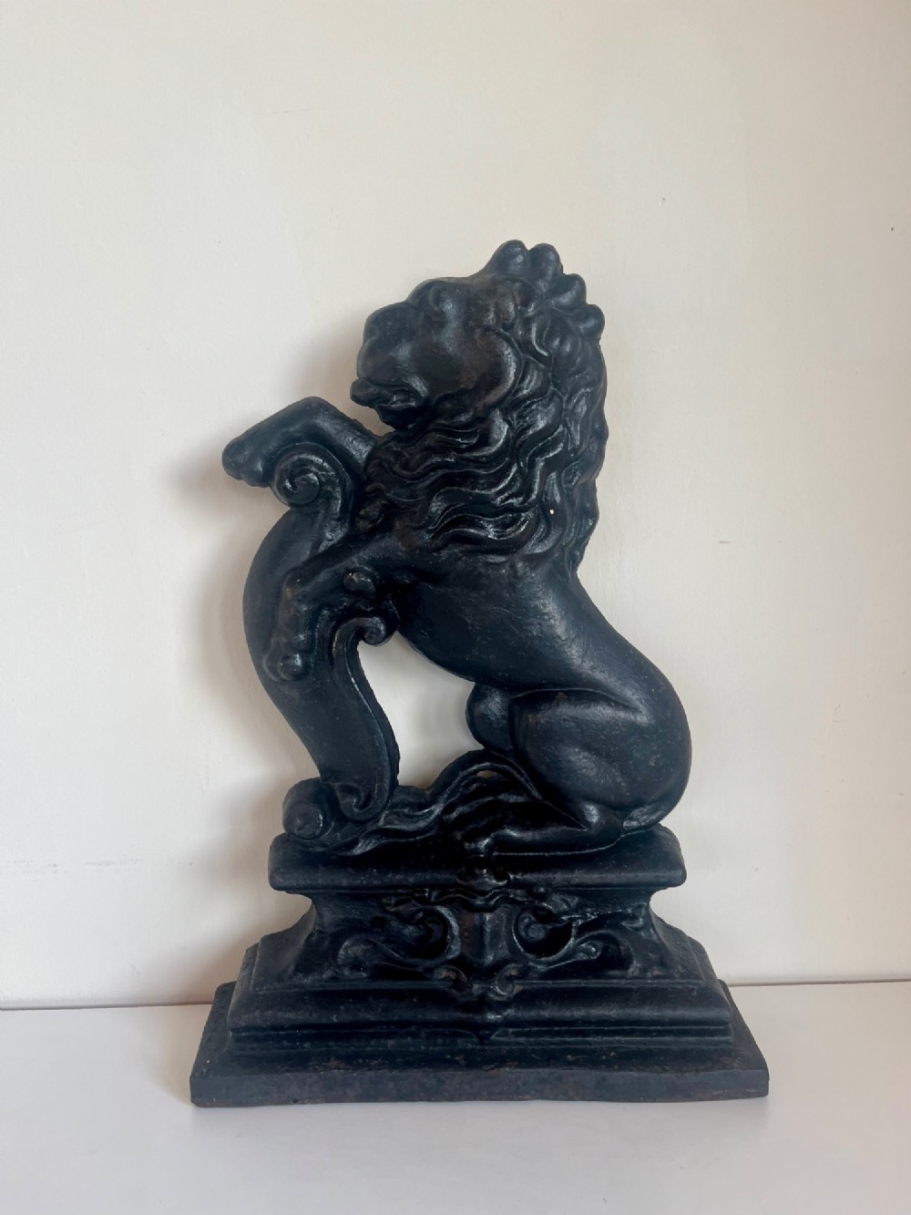 A heavy black cast iron door porter depicting a heraldic lion rampant on a stepped rectangular plinth base.
