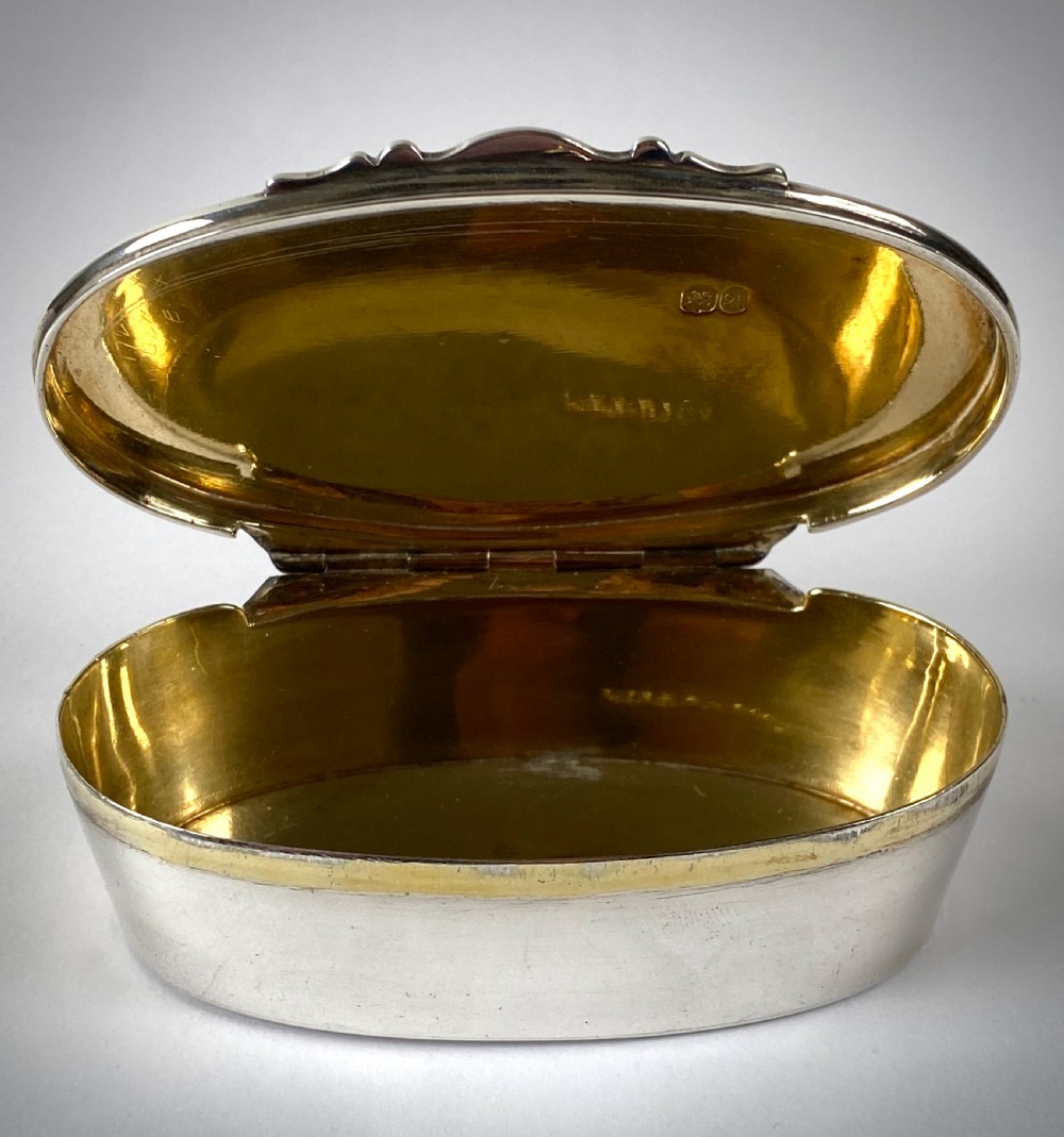 An open oval sterling silver snuff box displaying a gilded interior and hallmarks inside the lid.
