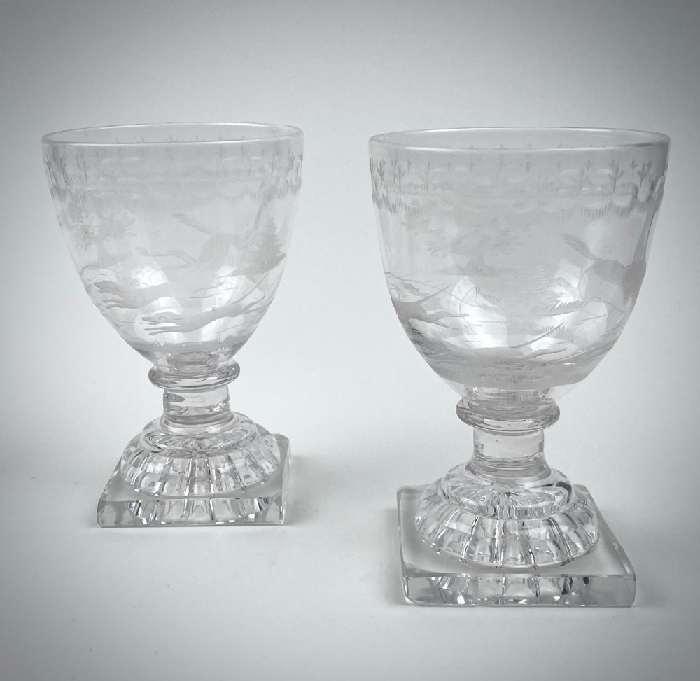 A pair of clear glass rummers featuring wheel-engraved fox hunting scenes set on square lemon squeezer bases. View II