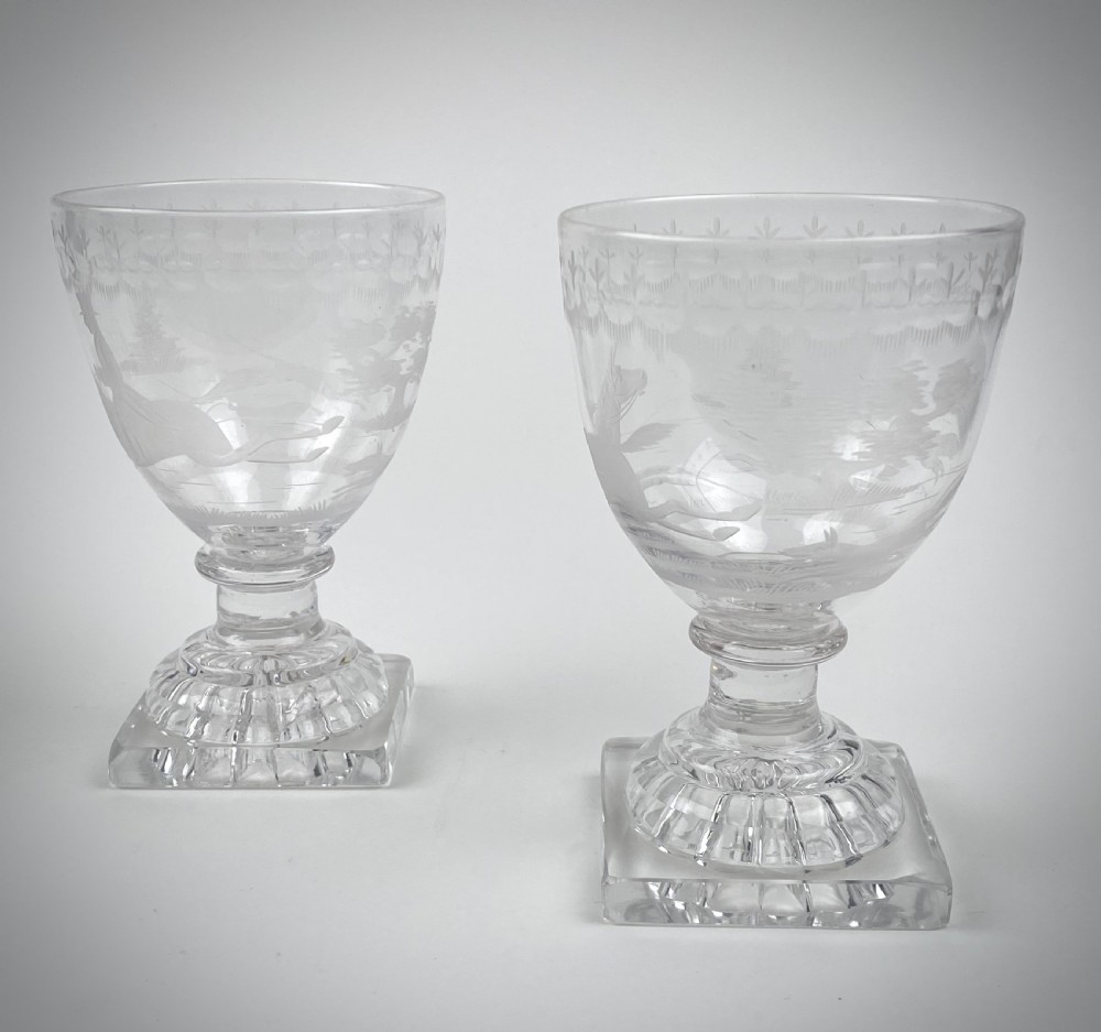 A pair of clear glass rummers featuring wheel-engraved fox hunting scenes set on square lemon squeezer bases. View III