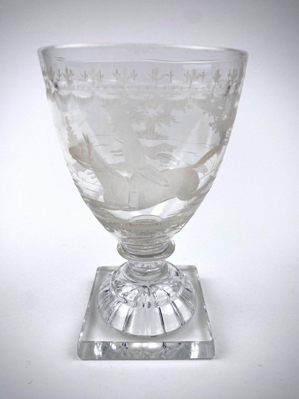 A clear Victorian glass rummer decorated with an engraved fox hunting scene, a short stepped stem, and a moulded square foot.