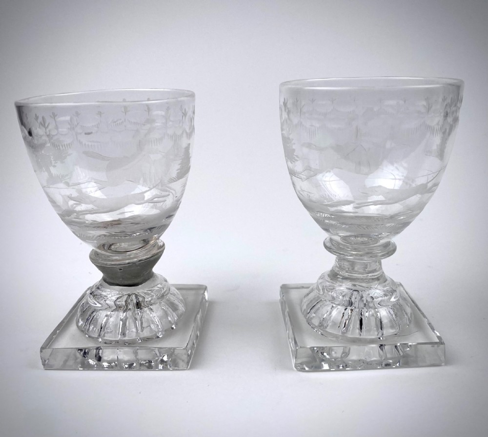 Clear glass rummer featuring an etched hunting scene of fox and hounds, supported by a ribbed stem and a square press-moulded lemon squeezer base. View VII