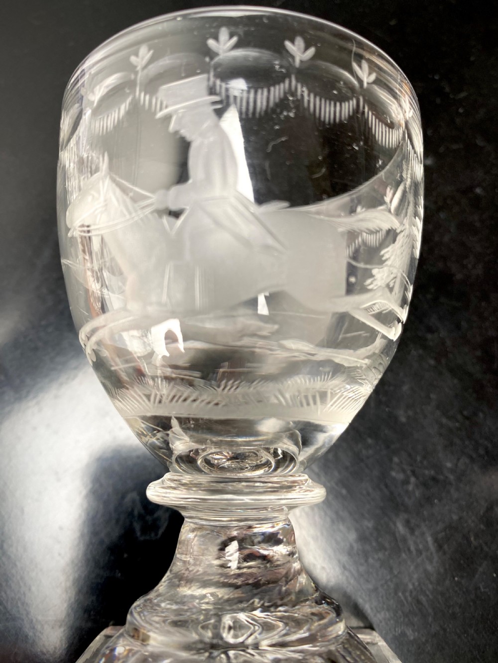 Clear glass rummer featuring an etched hunting scene of fox and hounds, supported by a ribbed stem and a square press-moulded lemon squeezer base. View IX