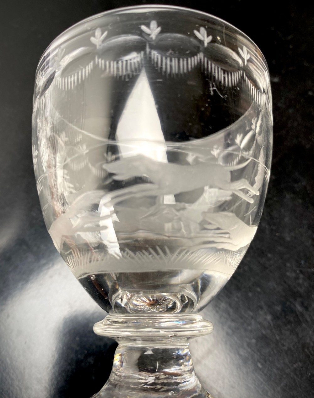 Clear glass rummer featuring an etched hunting scene of fox and hounds, supported by a ribbed stem and a square press-moulded lemon squeezer base. View XI