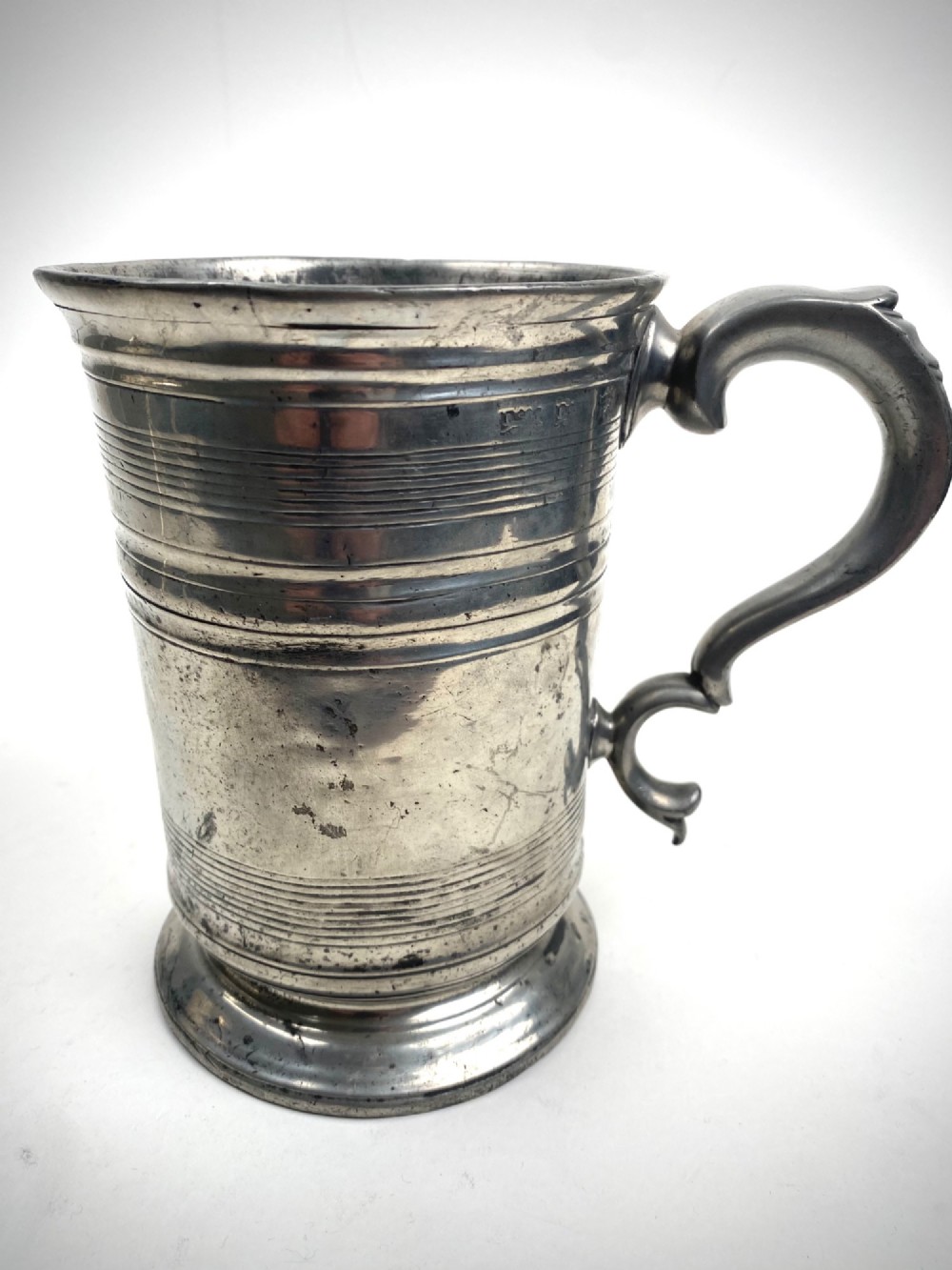 An eighteenth-century Georgian pewter quart tankard with horizontal reeded bands, a cast handle, and an engraved monogram on its grey surface. View II
