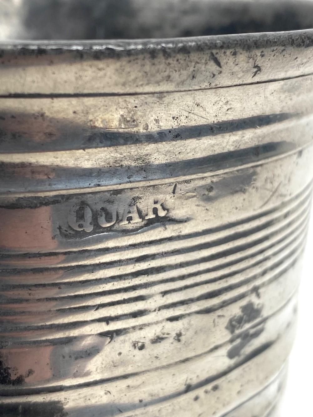 An eighteenth-century Georgian pewter quart tankard with horizontal reeded bands, a cast handle, and an engraved monogram on its grey surface. View III