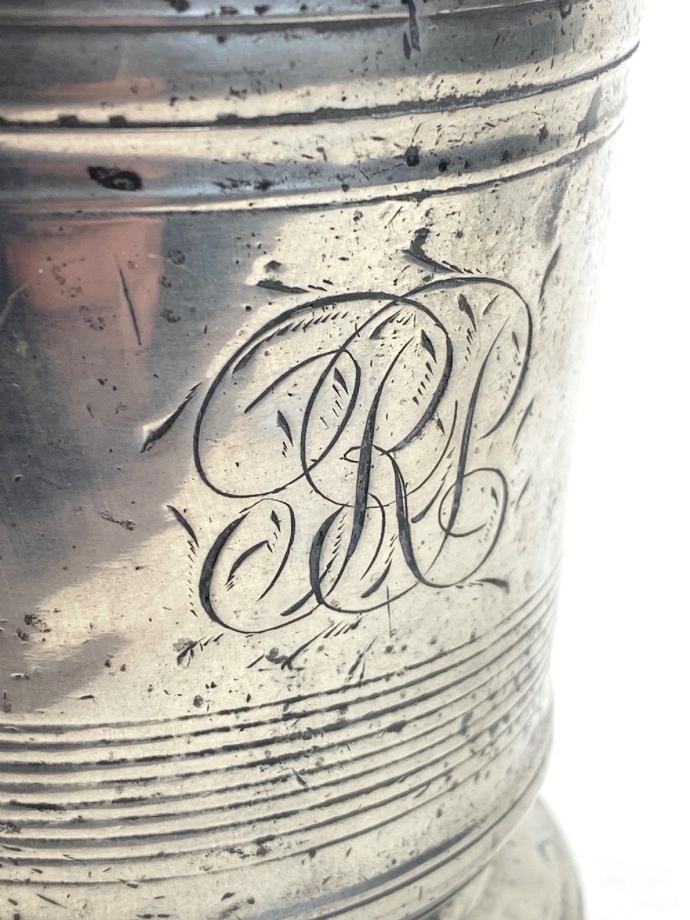 An eighteenth-century Georgian pewter quart tankard with horizontal reeded bands, a cast handle, and an engraved monogram on its grey surface. View IV