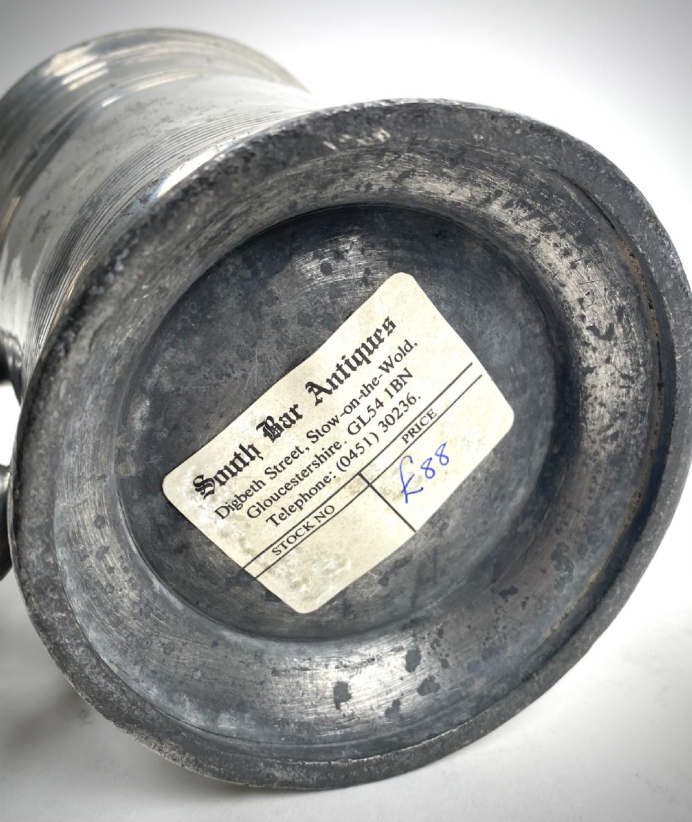 An eighteenth-century Georgian pewter quart tankard with horizontal reeded bands, a cast handle, and an engraved monogram on its grey surface. View VI