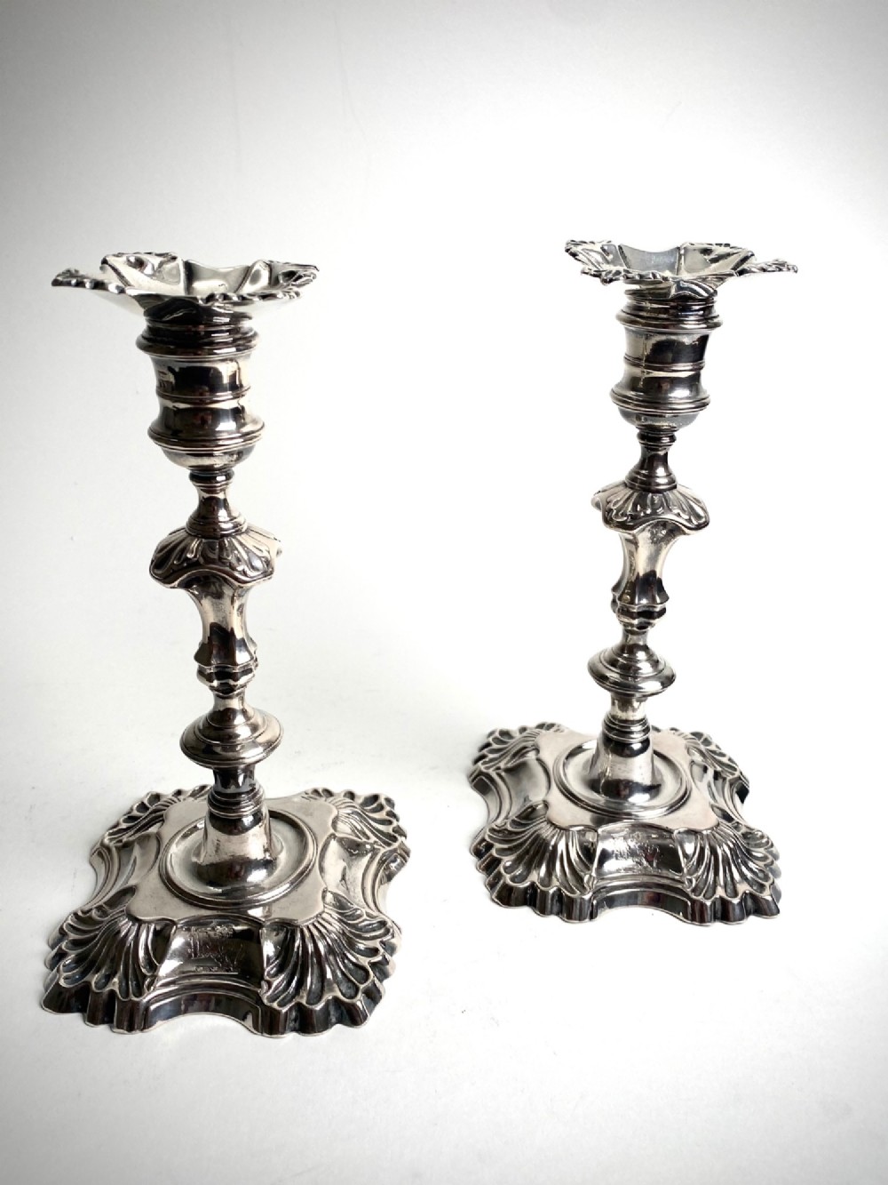 A pair of Georgian sterling silver candlesticks featuring shell-cast stepped bases and baluster stems.
