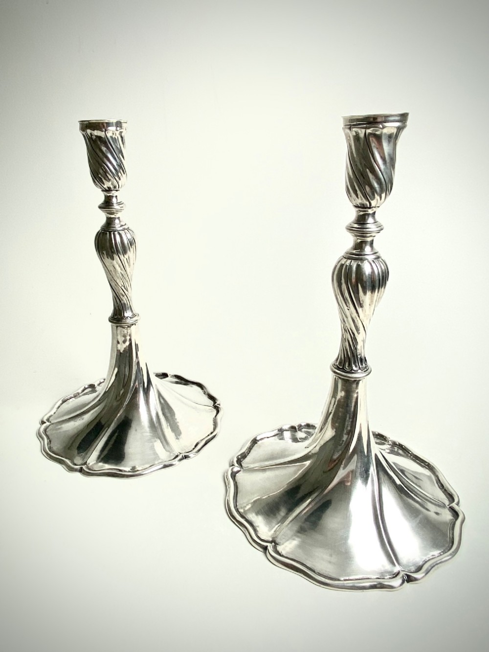 A pair of polished sterling silver candlesticks featuring spiral-twisted stems and wide, lobed flared bases.