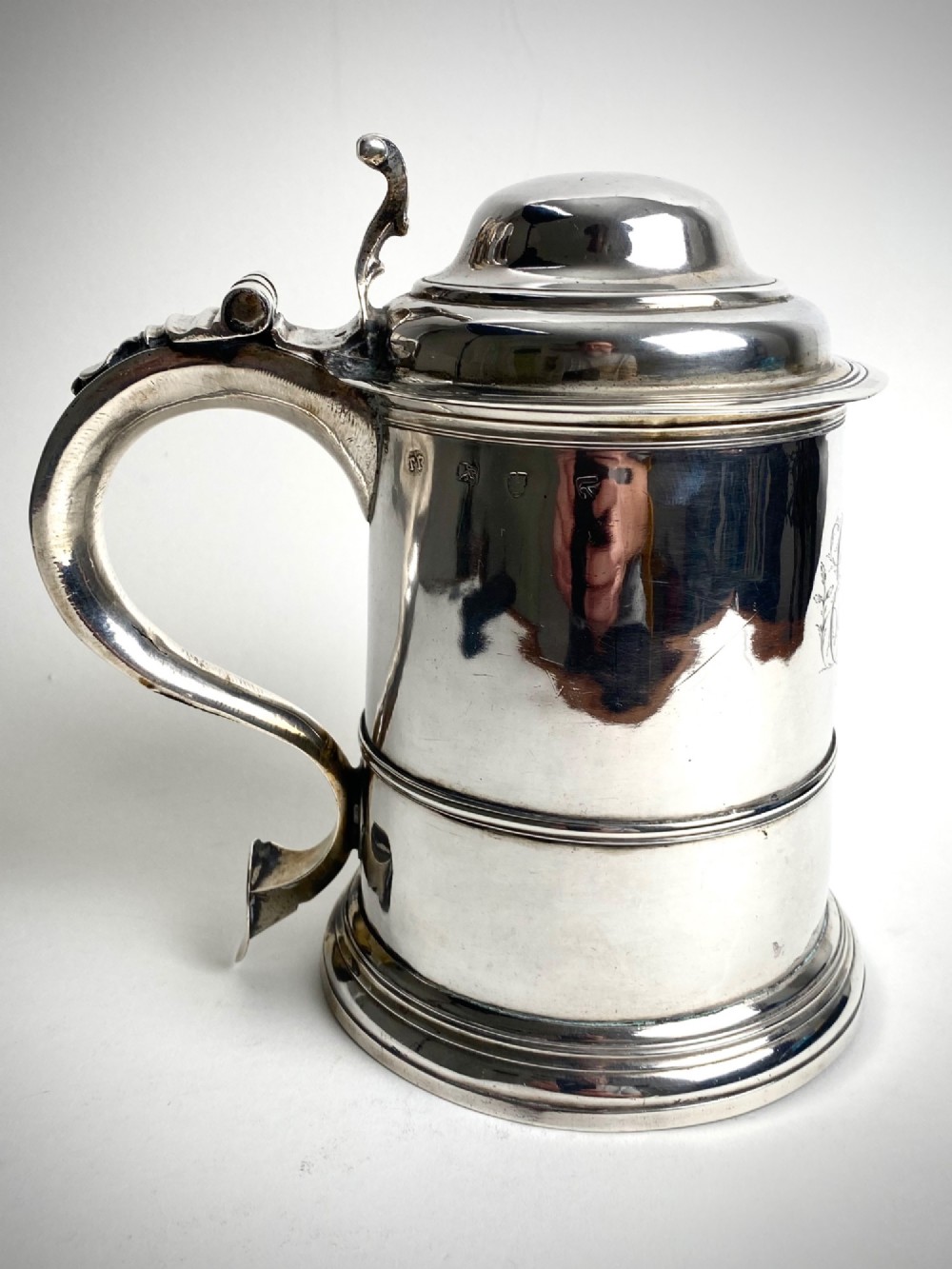 A Georgian sterling silver lidded tankard featuring a domed cap, thumbpiece, scrolled handle, and moulded girdle.