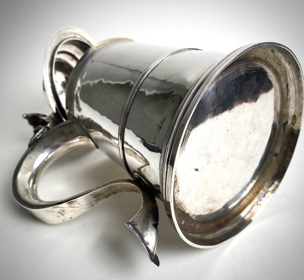A Georgian sterling silver lidded tankard featuring a domed cap, thumbpiece, scrolled handle, and moulded girdle. View IV