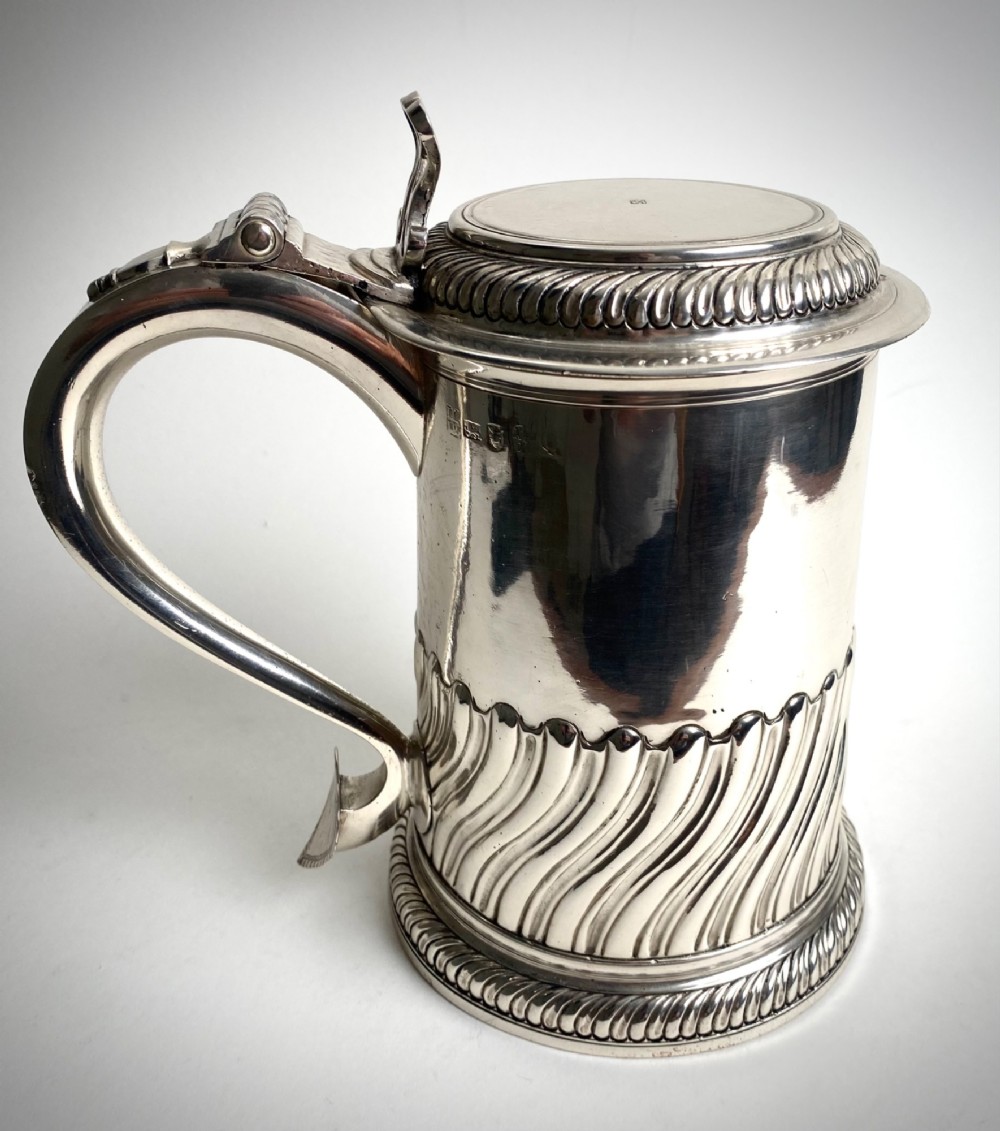 A sterling silver lidded tankard featuring spiralled fluted ornamentation along the lower body, gadrooned borders, a scroll handle, and stamped hallmarks.