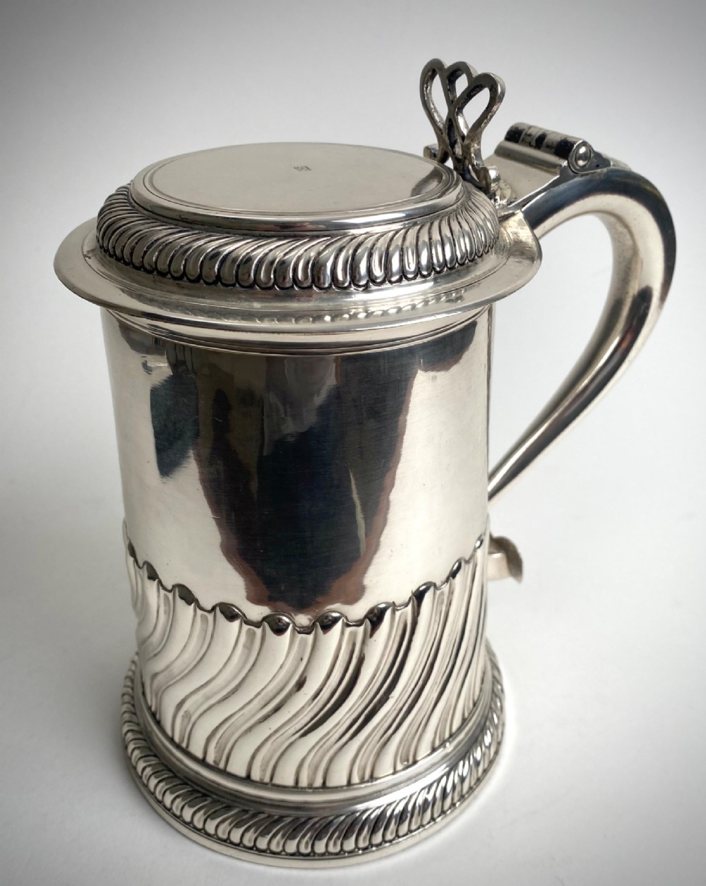A sterling silver lidded tankard featuring spiralled fluted ornamentation along the lower body, gadrooned borders, a scroll handle, and stamped hallmarks. View V