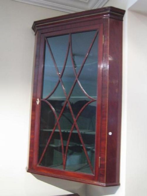fig 1. A wall-hanging Regency mahogany corner cabinet featuring a moulded cornice and a single door with curved astragal glazing bars.
