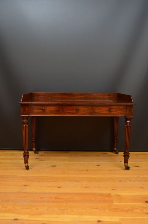fig 1. A mahogany writing table featuring three frieze drawers, a raised rear gallery upstand, reeded turned legs, and brass castors.