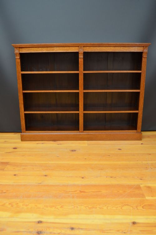fig 1. A wide Victorian oak open bookcase featuring two bays with four tiers of shelves filled with books and carved floral pilaster details.