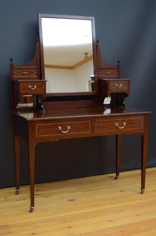 fig 1. An Edwardian mahogany dressing table featuring a central rectangular mirror, side trinket drawers with fretwork panels, two main frieze drawers with brass handles, and square tapered legs on castors.