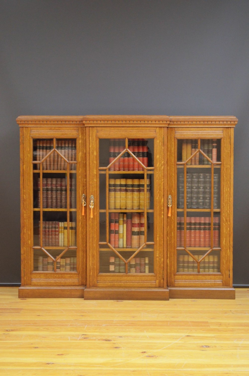 A Victorian three-door breakfront oak bookcase featuring geometric glazed doors and brass escutcheons.