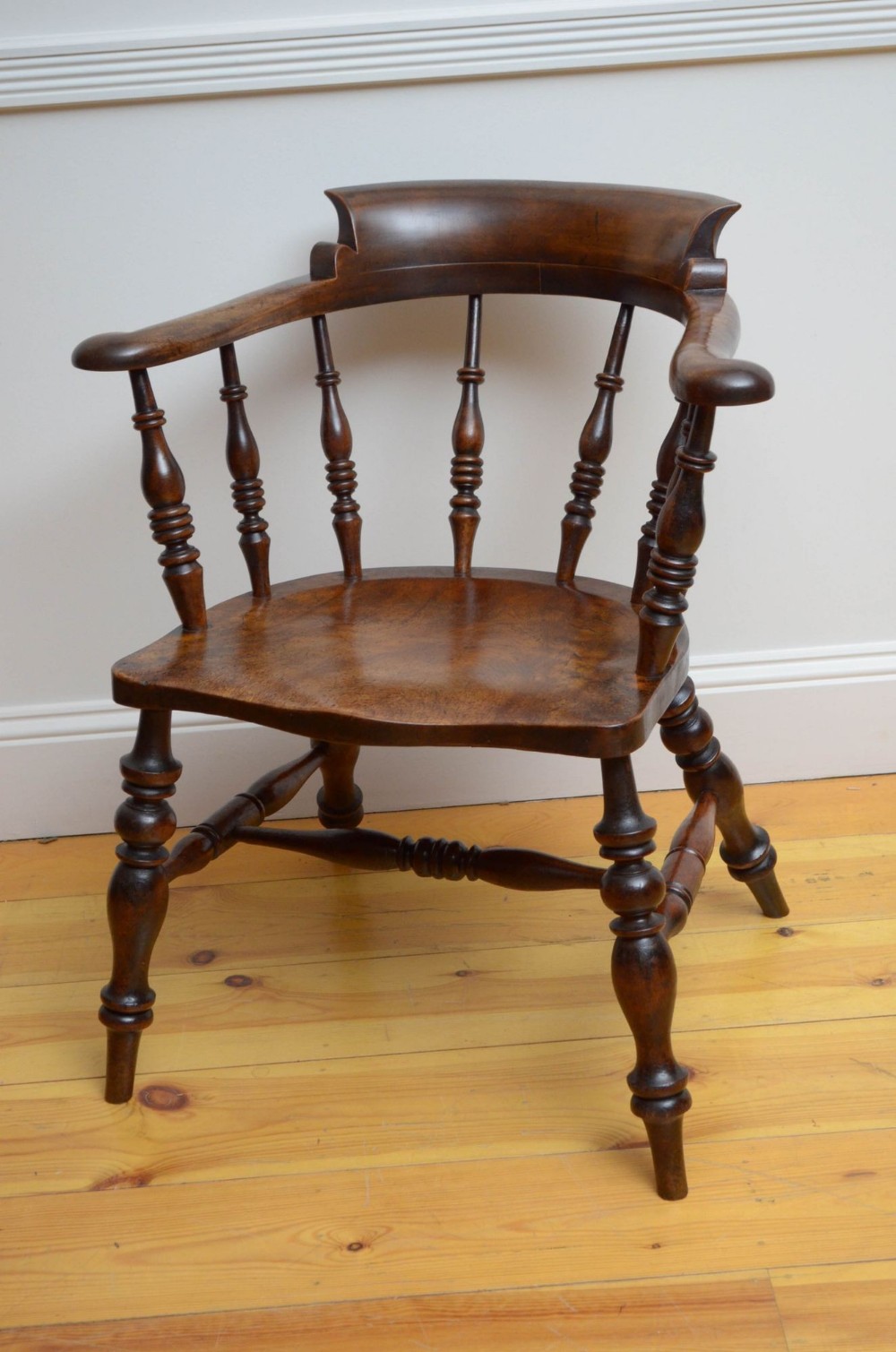 A dark polished Victorian smokers bow wooden armchair featuring turned spindles, a curved horseshoe armrest, and a shaped solid seat.