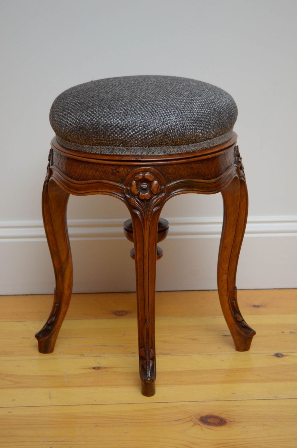 A French walnut revolving piano stool featuring carved cabriole legs with floral knees and a cushioned round seat upholstered in grey fabric.