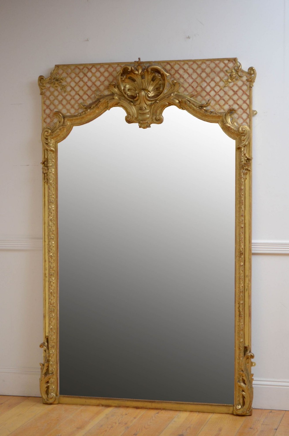 A tall 19th-century French trumeau mirror featuring a gilded carved frame with a shell motif crest and lattice-patterned top panel.