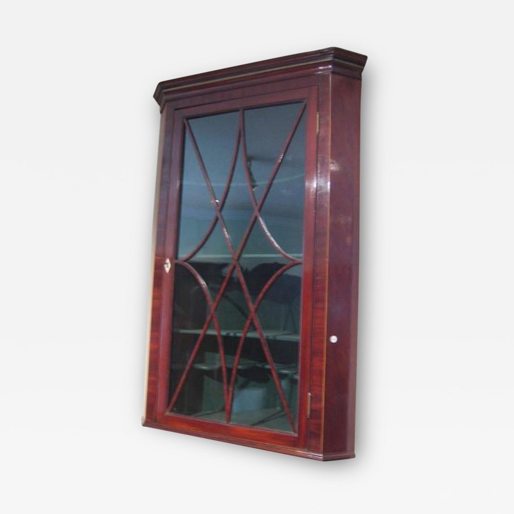 A wall-hanging Regency mahogany corner cabinet featuring a moulded cornice and a single door with curved astragal glazing bars.