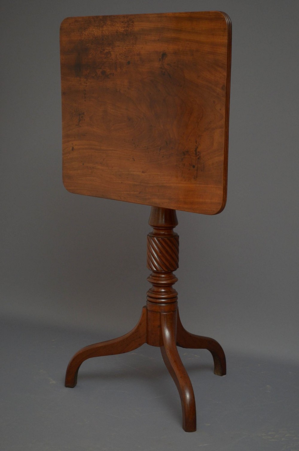 A Regency mahogany tilt-top occasional table shown with its rectangular top locked in a vertical position, featuring a spiral-carved central pedestal and a tripod base.