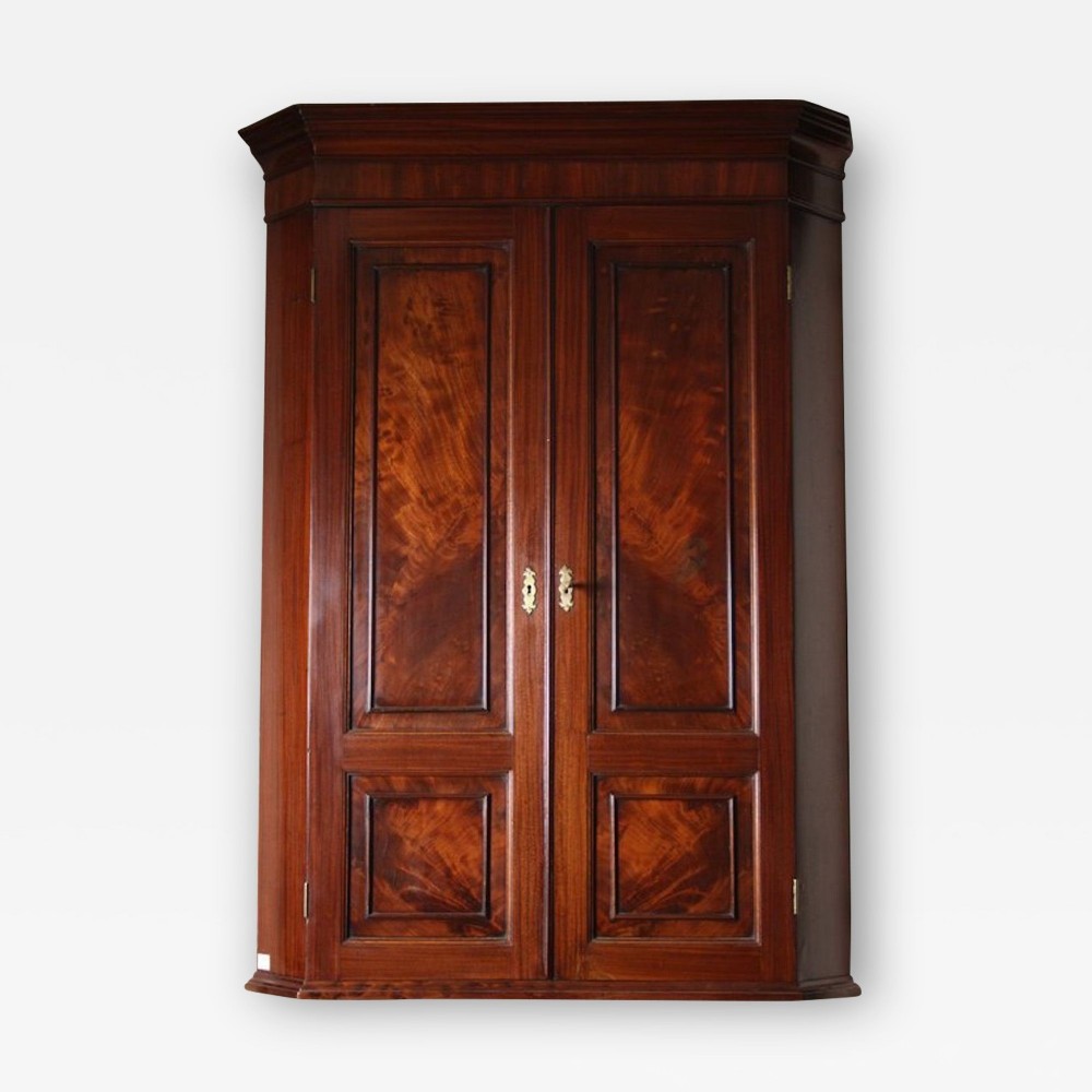 A Regency flame mahogany corner cupboard featuring double panelled doors, brass escutcheons, and a moulded cornice.