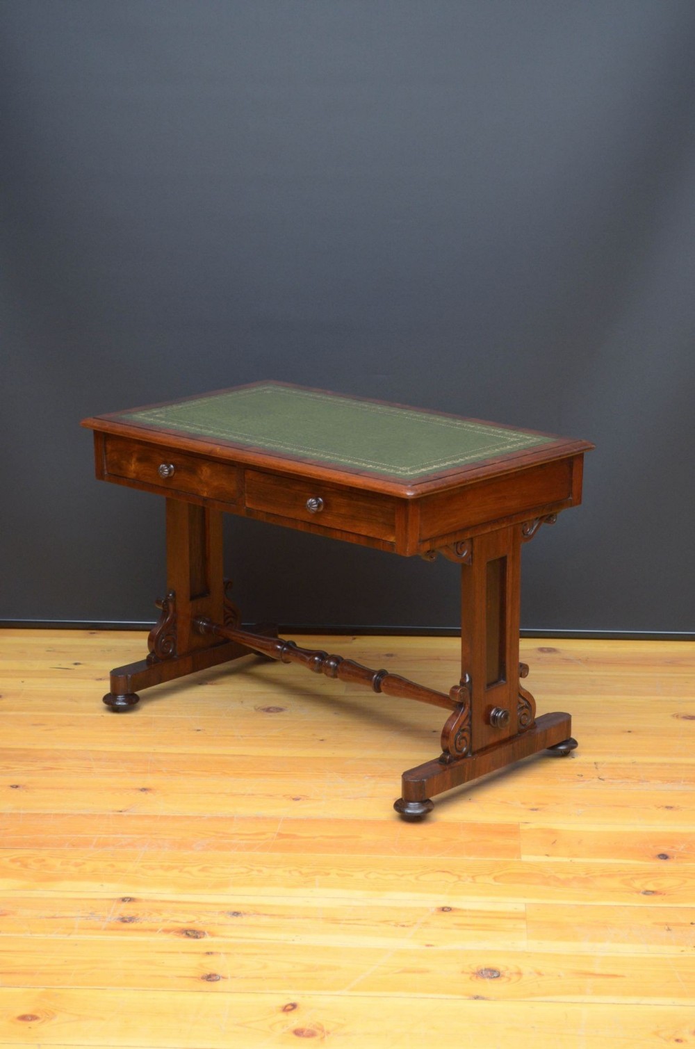 A William IV rosewood library table with a green gilt-tooled leather writing surface, twin frieze drawers, scroll brackets, and a turned stretcher rail.