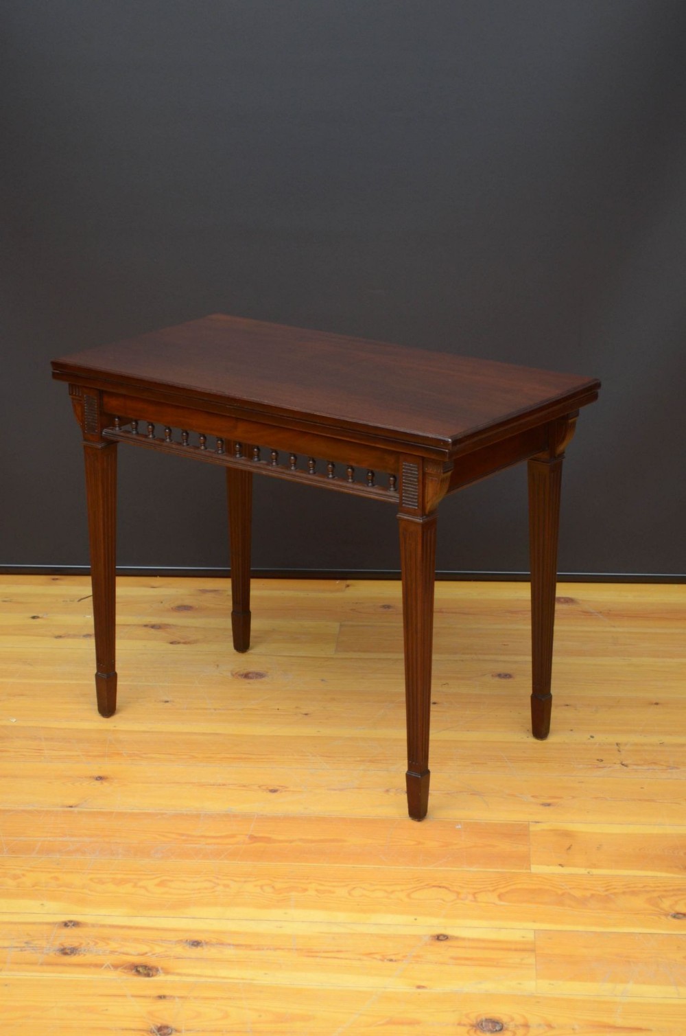 A mahogany foldover card table featuring a rectangular top, a spindled gallery frieze, and four tapered fluted legs.