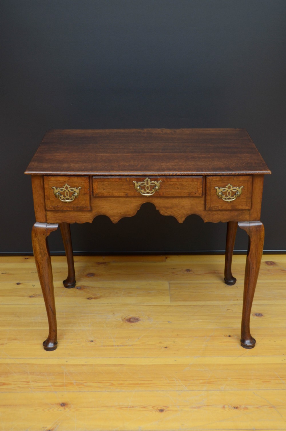 An 18th-century George II oak lowboy table featuring three drawers with decorative brass handles, a shaped lower apron, and four cabriole legs with pad feet.