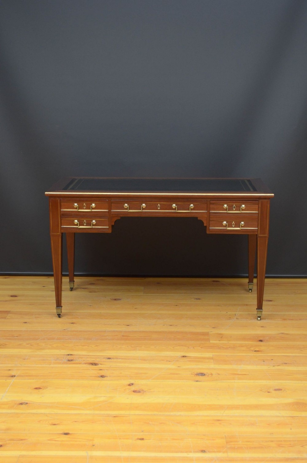 A 19th-century mahogany writing table featuring a dark leather inset top, brass-trimmed drawers with ring handles, tapered legs, and brass castors.