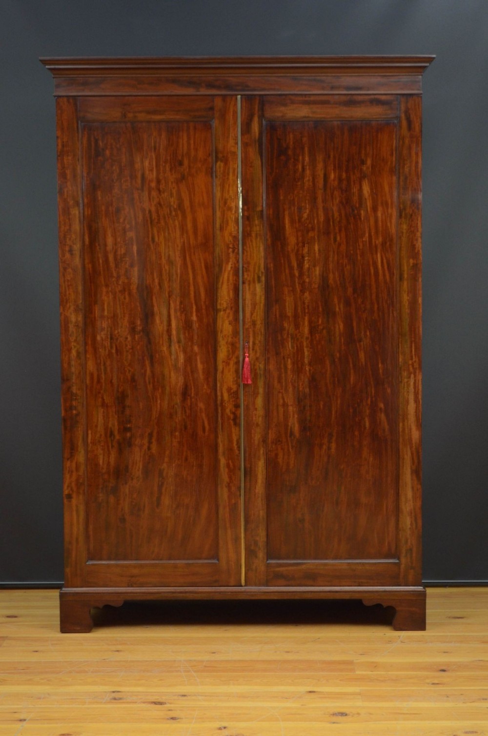 A George IV flame mahogany two-door wardrobe featuring flat panel doors, a moulded cornice, and bracket feet.