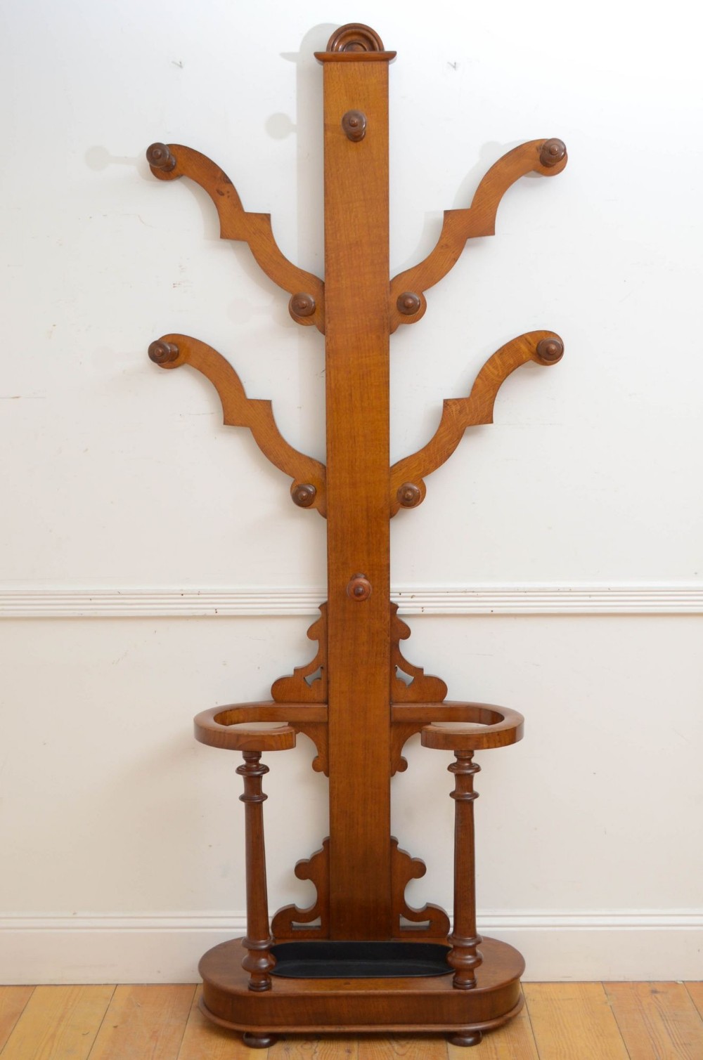 A Victorian oak hall stand featuring curved coat branches with wooden pegs, turned support columns, and an integrated umbrella rack with a removable drip tray.