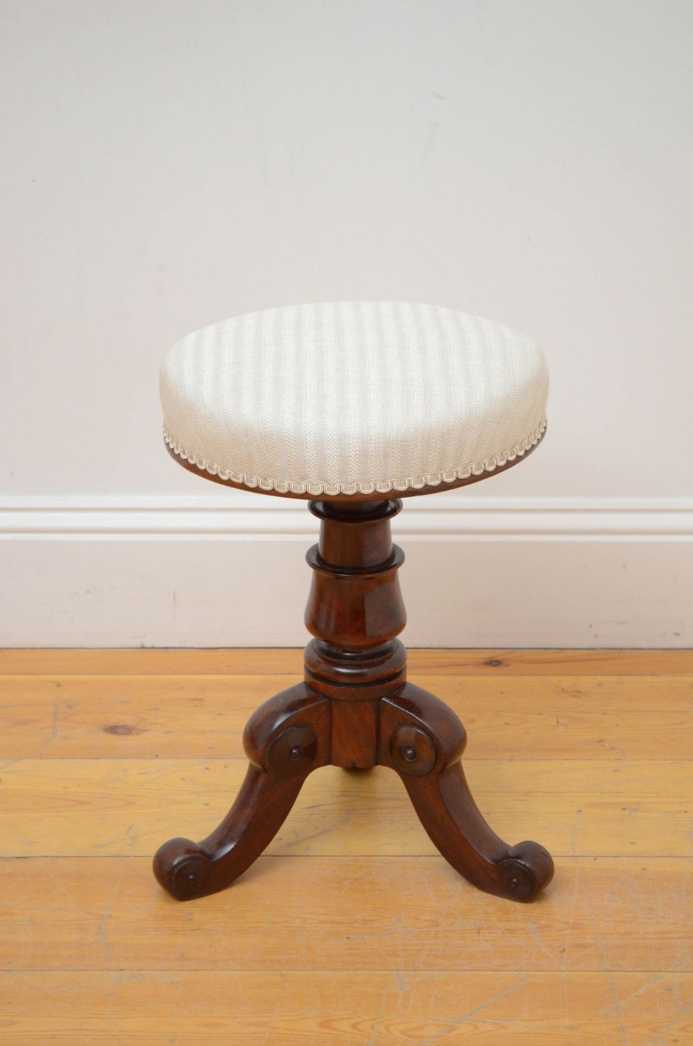 A William IV mahogany revolving piano stool with a circular cream striped upholstered seat, turned central column, and tripod scroll feet.