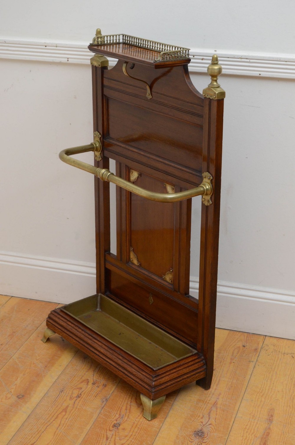 A Victorian oak umbrella stand featuring a top shelf with a brass gallery rail, a central wood panel, a curved brass retaining bar, and a fitted brass drip tray at the base.