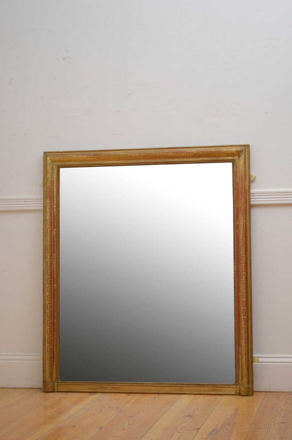 A large 19th-century rectangular wall mirror featuring a gilded frame decorated with a carved Greek key motif and beaded inner border.