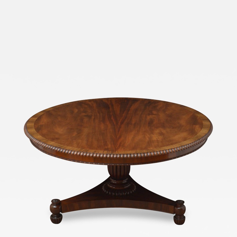 A circular Regency mahogany centre table featuring flame mahogany veneer, a reeded edge, and a fluted central pedestal column on a triform base.